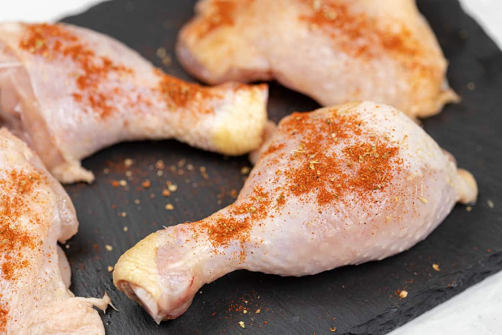 Chicken legs with sprinkled paprika and ground thyme on them, ready for cooking